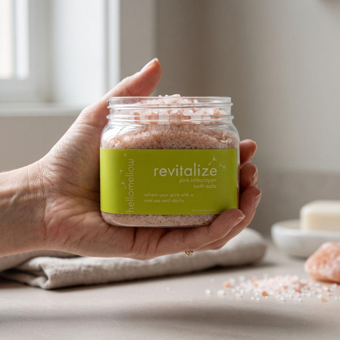 adult hand holding the revitalize bath salts jar with the label facing forward