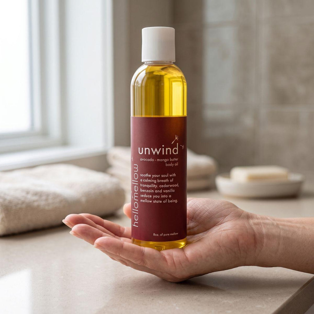 adult hand holding the unwind body oil bottle with the label facing forward