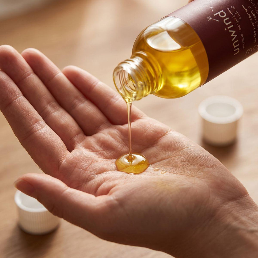 unwind body oil pouring into an open palm with the bottle nearby
