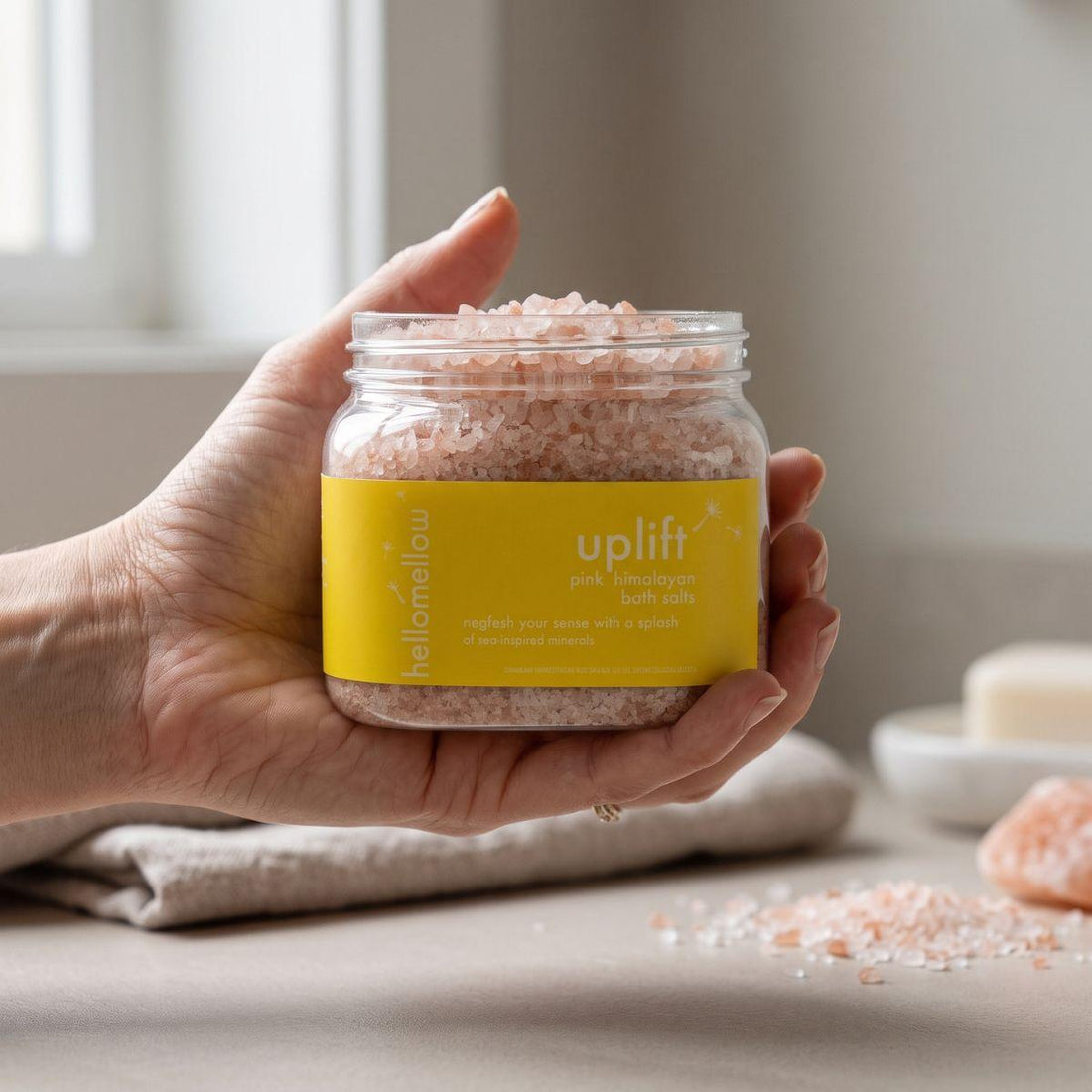 adult hand holding the uplift bath salts jar with the label facing forward