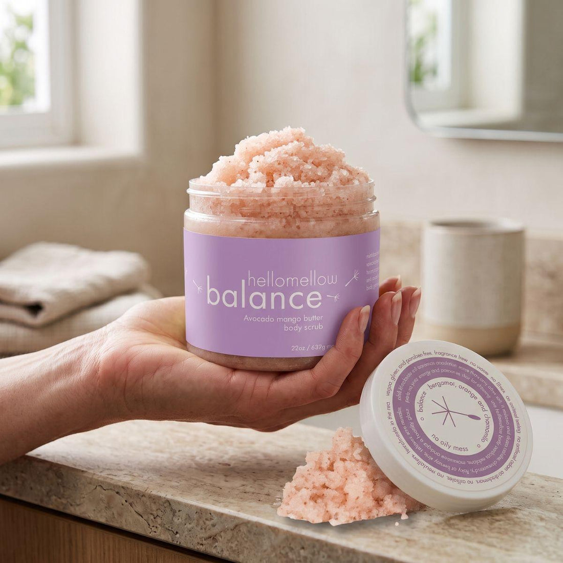 adult hand holding the balance body scrub jar with the label facing forward