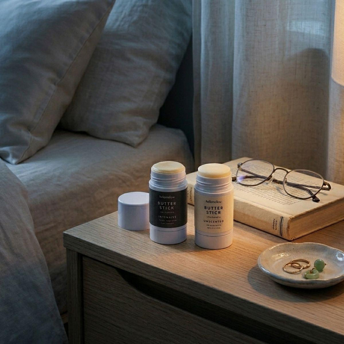 butter stick duo one unscented butter stick and one intensive butter stick pictured on a nightstand in dim lighting 