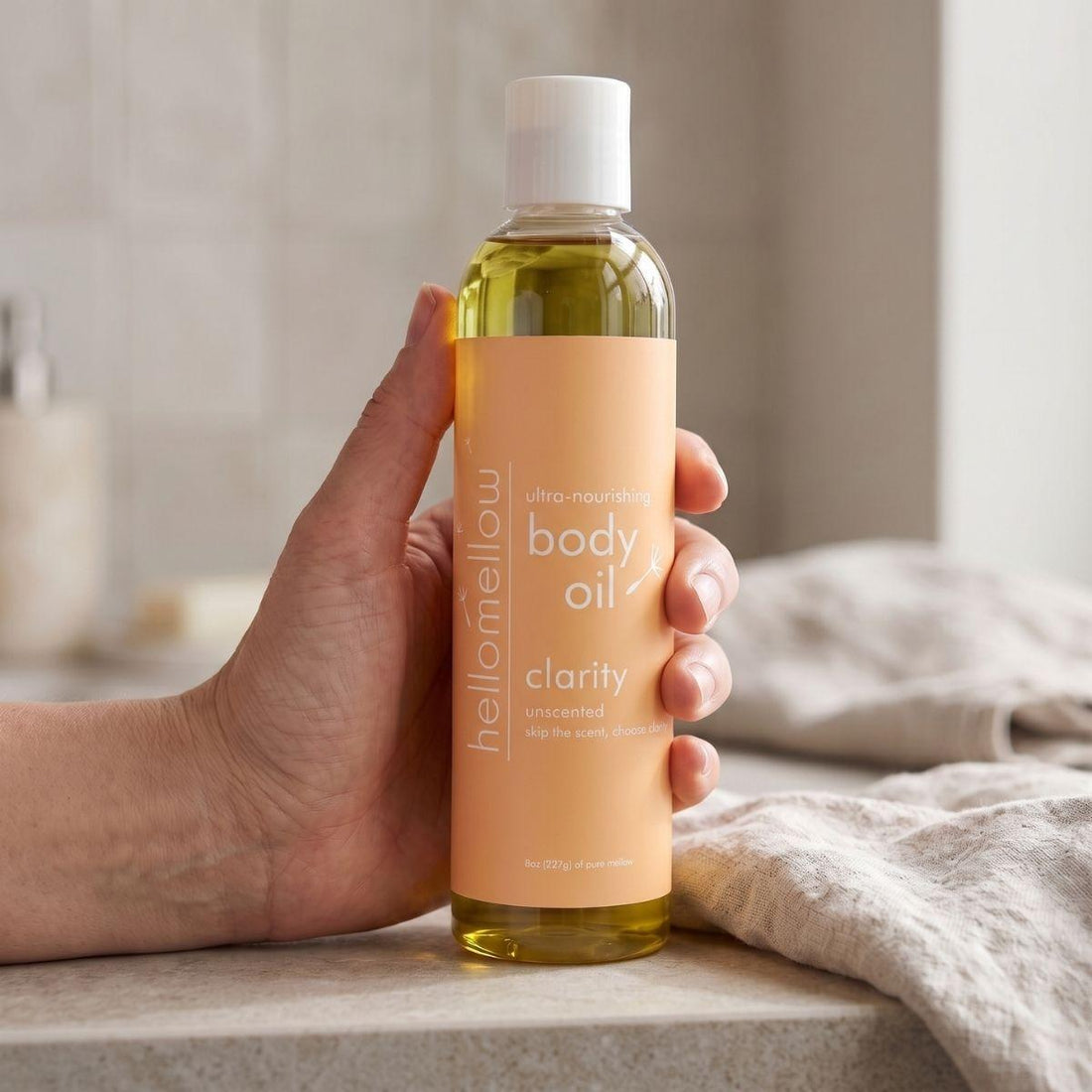adult hand holding the clarity body oil bottle with the label facing forward