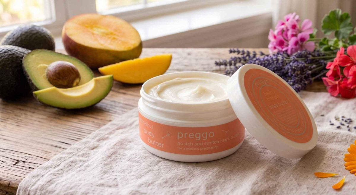 open preggo body butter with avocado, mango, lavender and geranium arranged on a softly lit table.