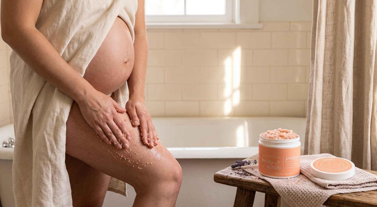 pregnant woman gently exfoliating her thigh with body scrub beside a softly lit bathtub.