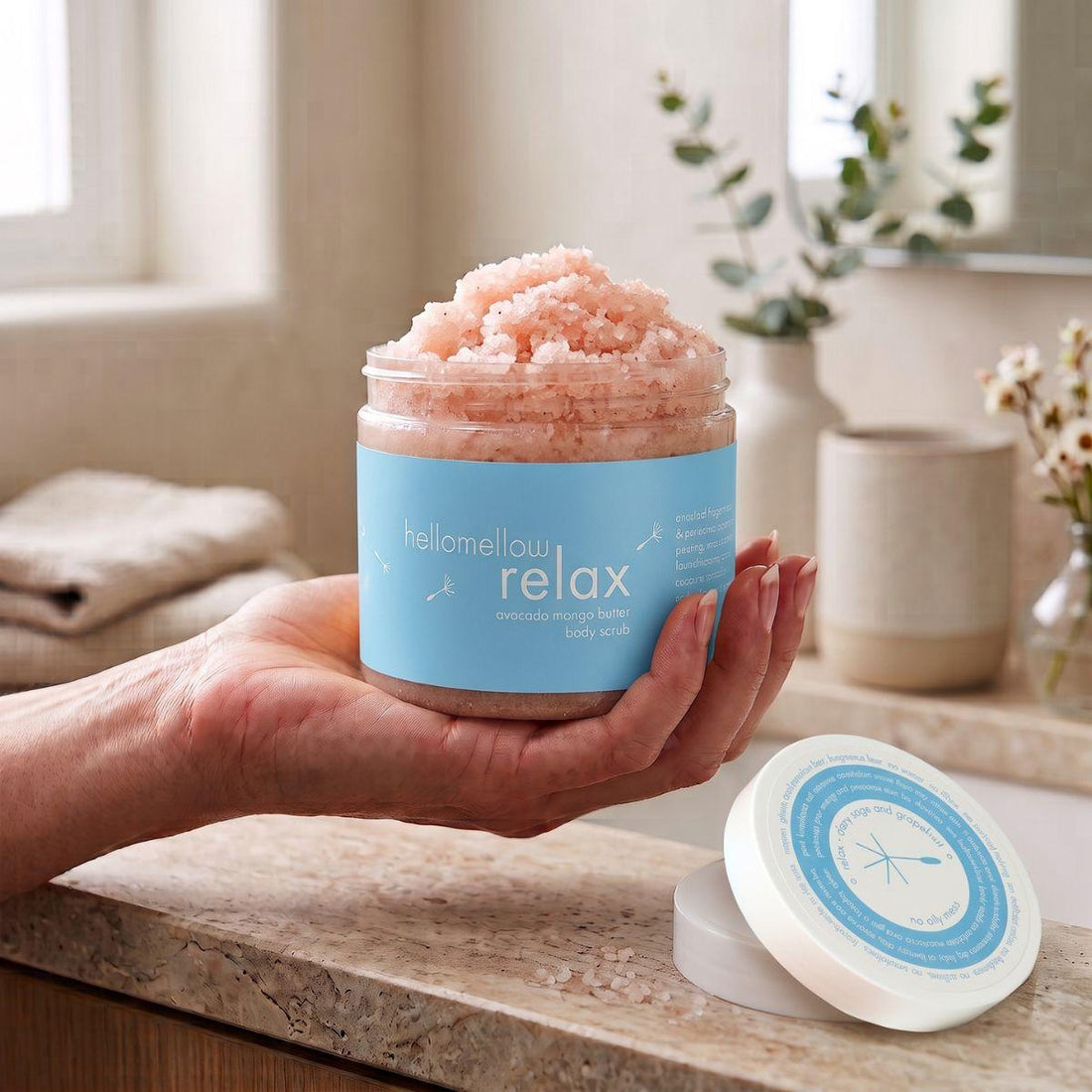 adult hand holding the relax body scrub jar with the label facing forward