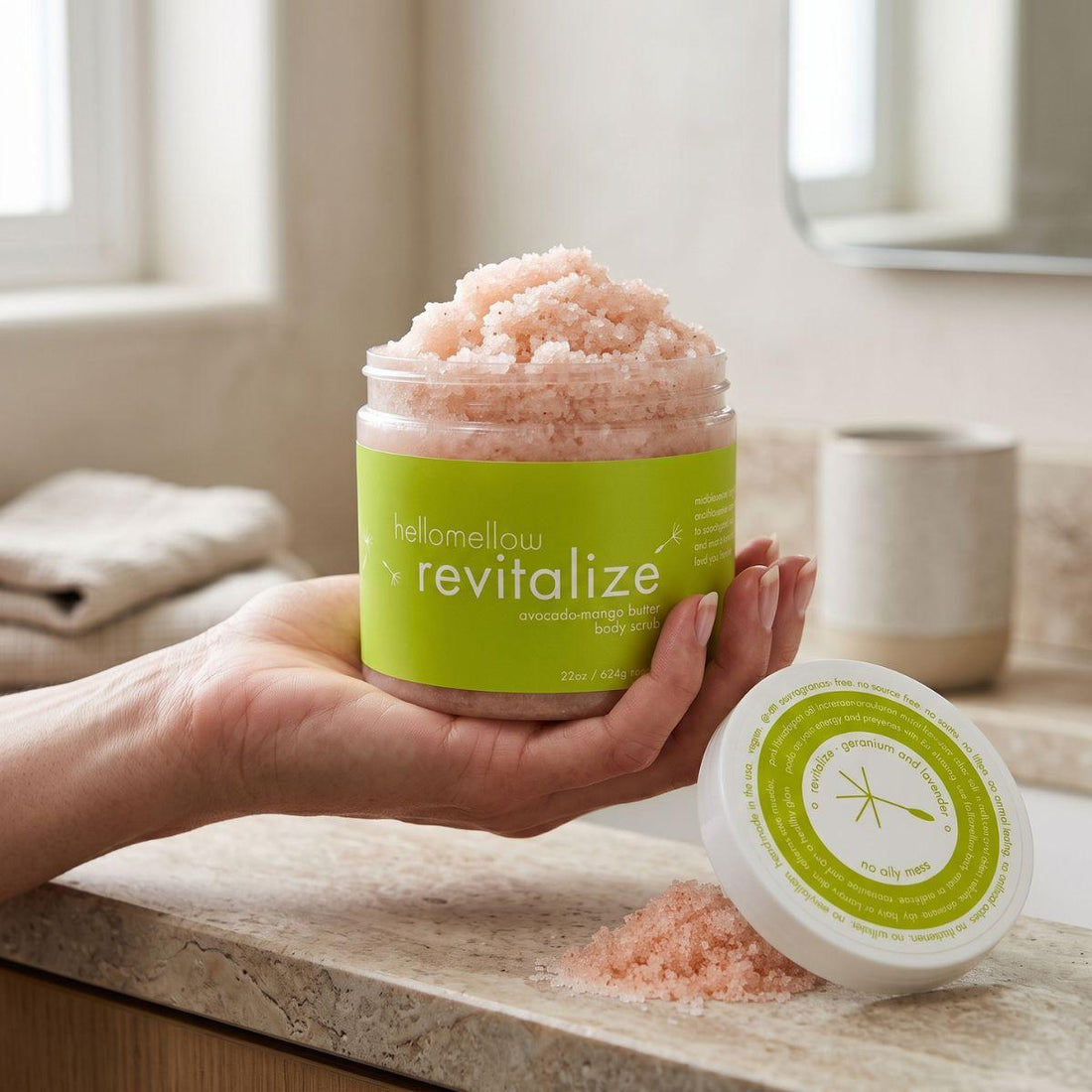 adult hand holding the revitalize body scrub jar with the label facing forward