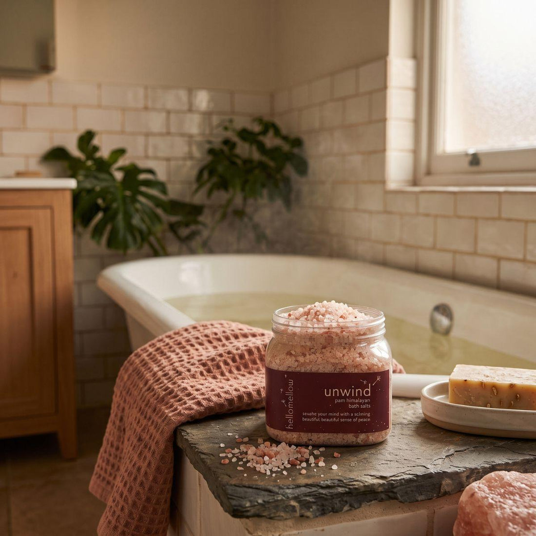 unwind bath salts beside a warm bath with a folded towel nearby