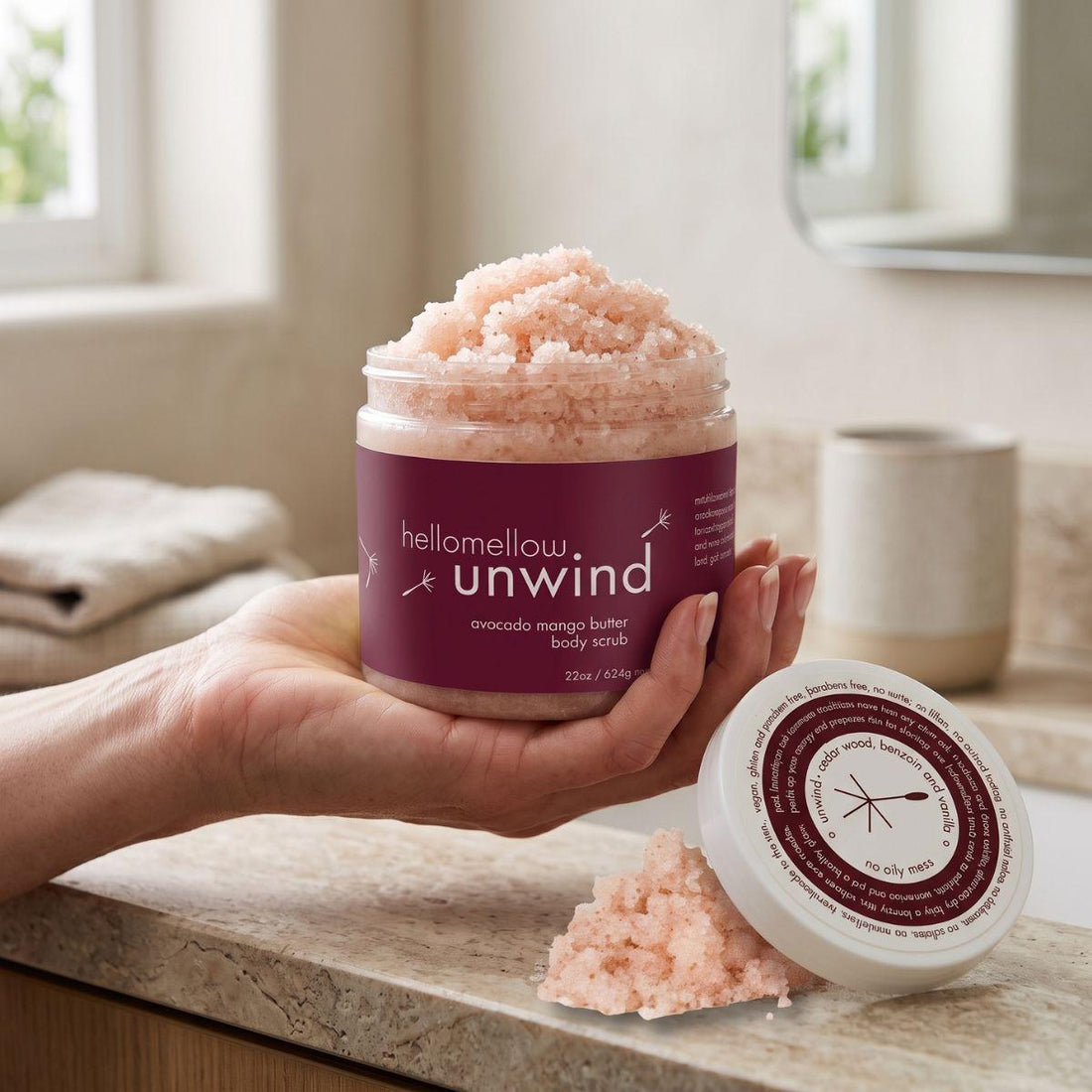 adult hand holding the unwind body scrub jar with the label facing forward