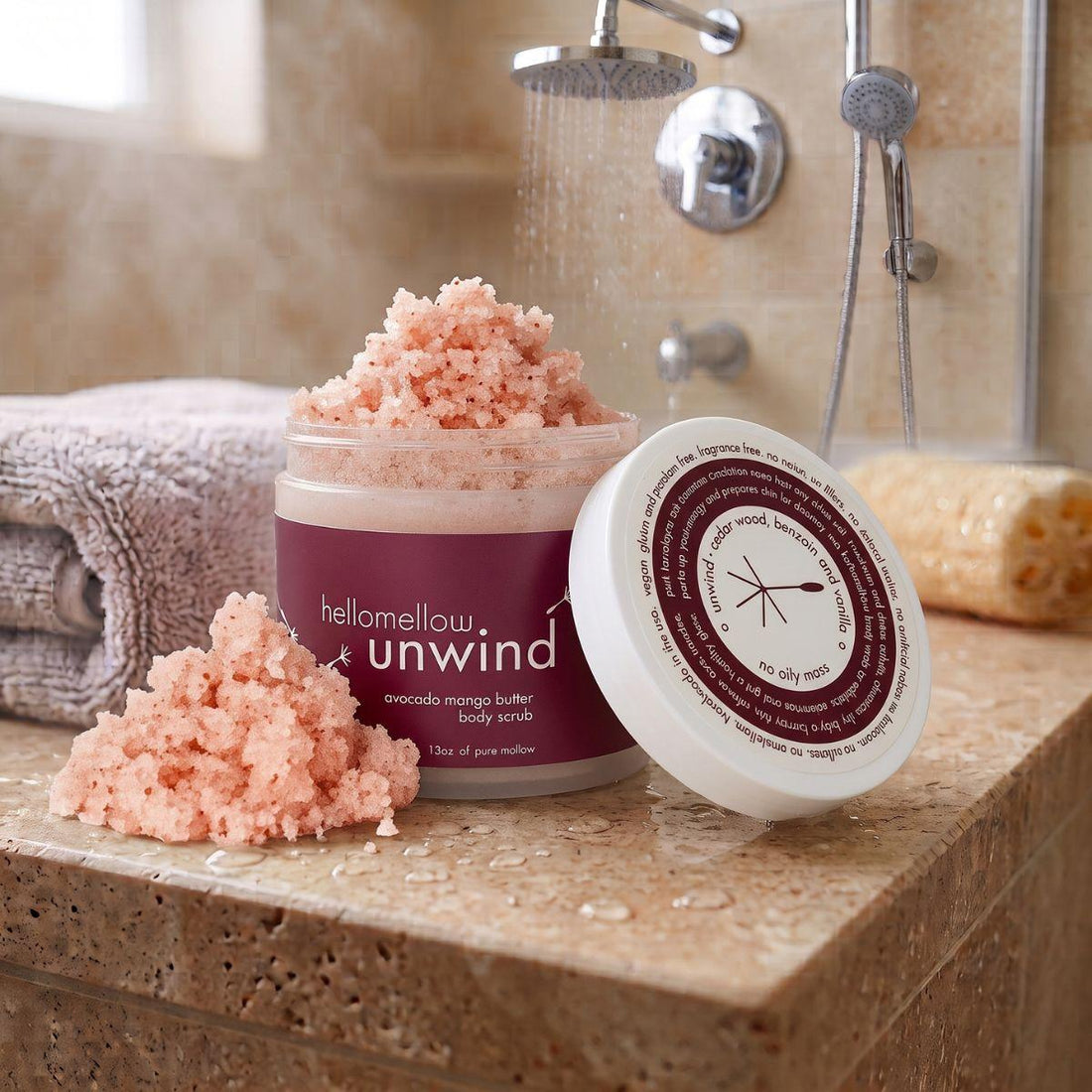unwind body scrub on a shower ledge beside a folded towel