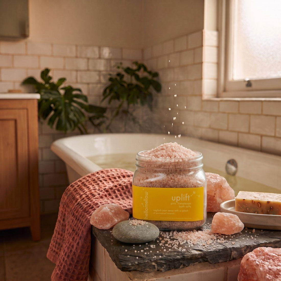uplift bath salts beside a warm bath with a folded towel nearby
