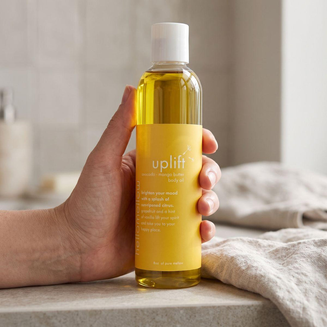 adult hand holding the uplift body oil bottle with the label facing forward